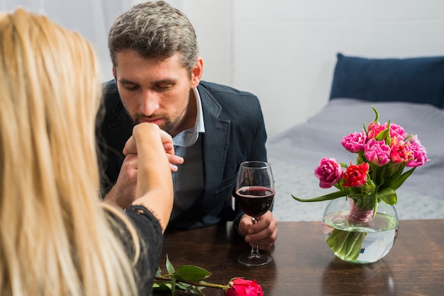 Man with glass of wine kissing hand of woman at table