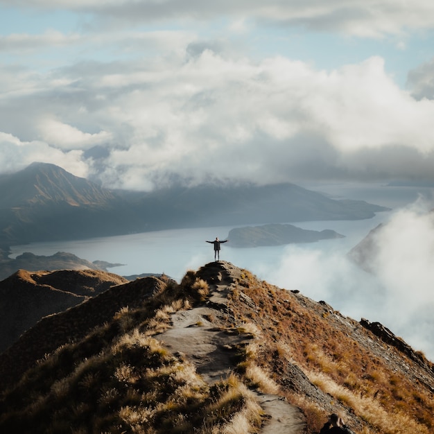 Man with hands wide open standing at the top of a mountain enjoying the incredible view of a lake