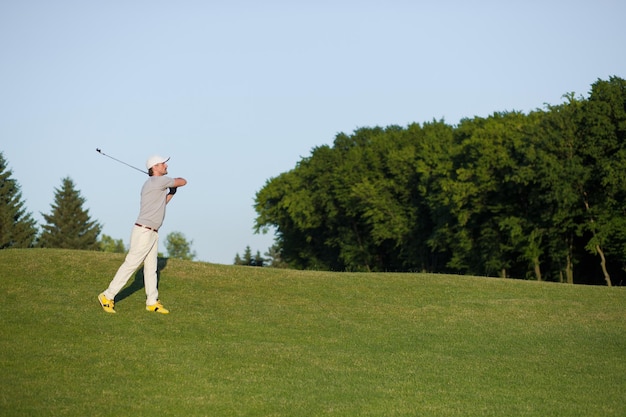 Man with hat on playing professional golf in the air. Golfer hitting golf shot with club on the course.