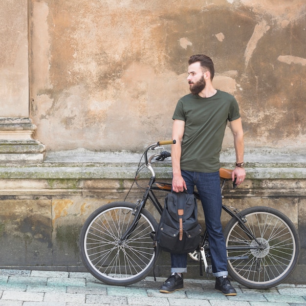 Free photo man with his bicycle standing in front of old wall