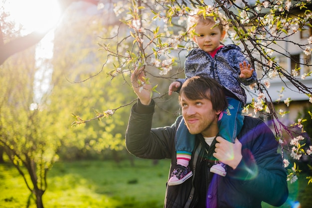 Free Photo man with his son on his shoulders and touching a branch