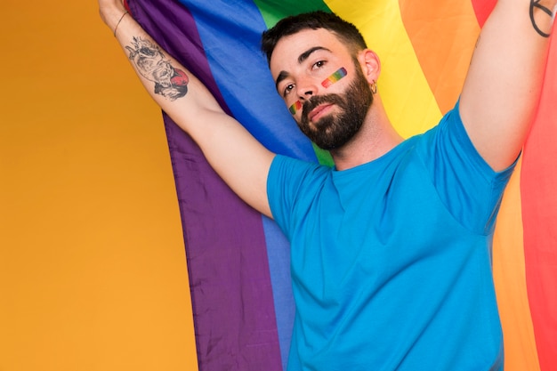 Free photo man with lgbt rainbow on face with multicolored flag