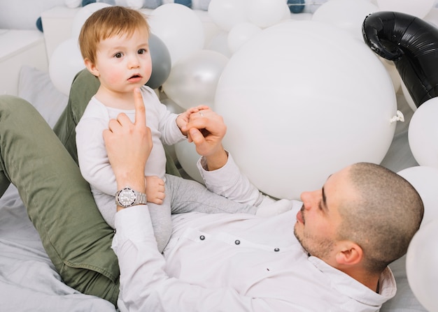 Man with little baby playing on bed near balloons