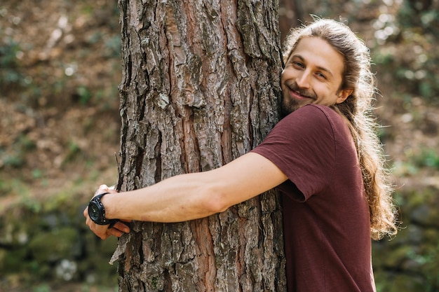 Man with long hair hugging a tree