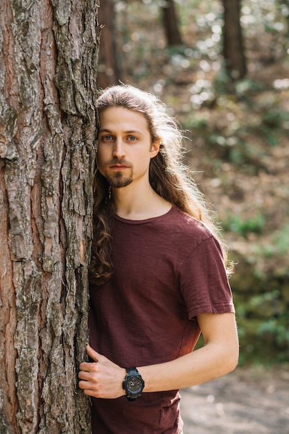 Free photo man with long hair hugging a tree