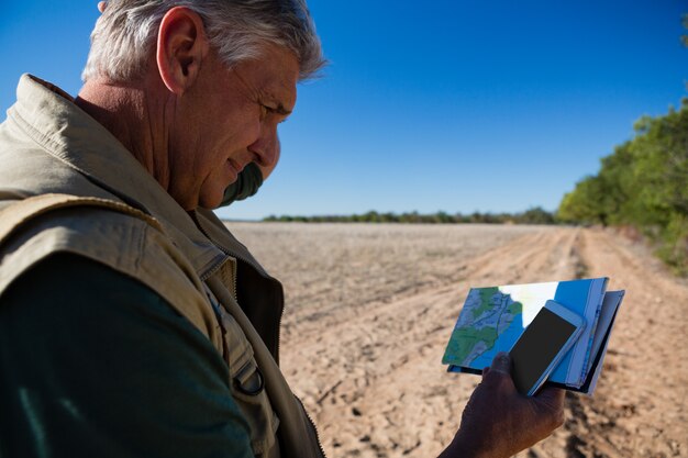 Man with map using phone on field