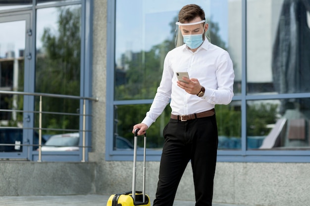 Man with mask and luggage checking phone