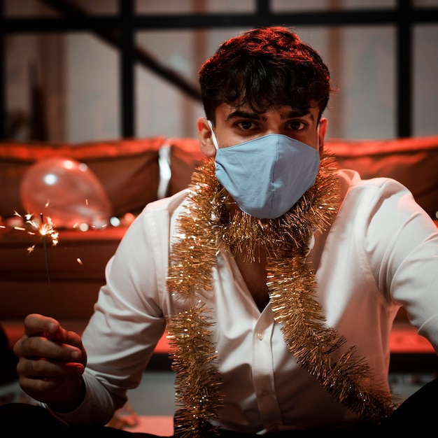 Free Photo man with medical mask holding a sparkler at new year's eve party