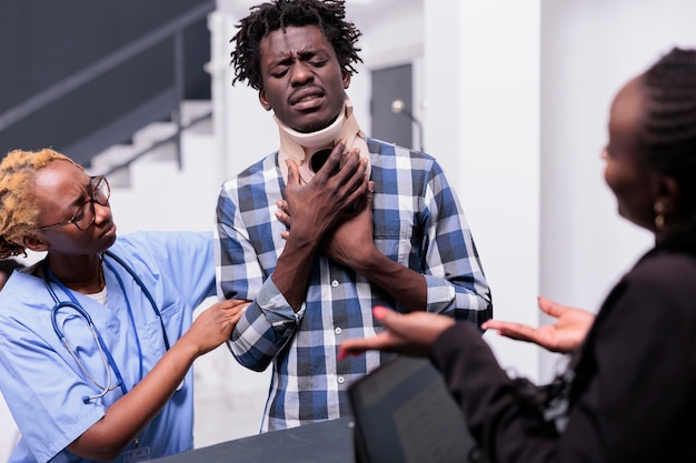 Man with medical neck brace receiving support and help from nurse and receptionist, giving treatment to cure pain aftter accident injury. Person wearing cervical collar foam in hospital reception.