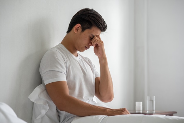 A man with migraines holds her hand by his nose in the bed.