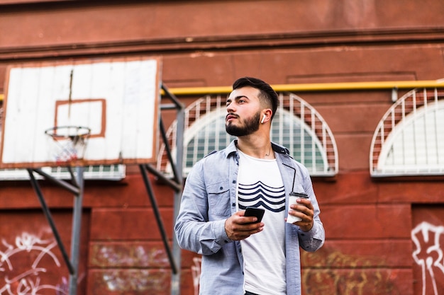 Free photo man with mobile phone standing in basketball court