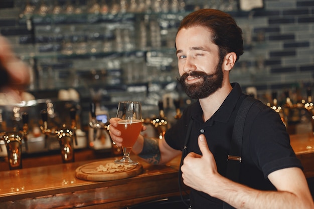 Free photo man with a mustache and beard stands at the bar and drinks alcohol from a glass.