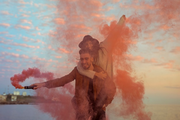 Man with red smoke bomb holding woman on back 