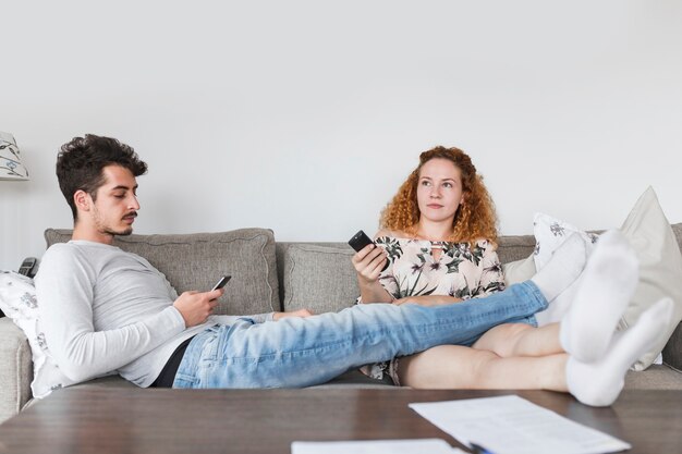 Man with smartphone sitting near her wife watching television