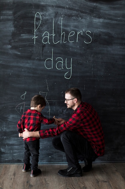 Free photo man with son on fathers day in front of chalkboard