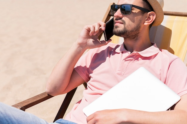 Man with sunglasses at the beach with laptop and smartphone