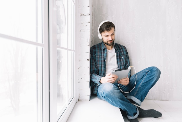 Free Photo man with tablet relaxing near window