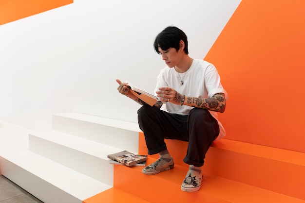 Man with tattoos drinking coffee and reading book at cafe