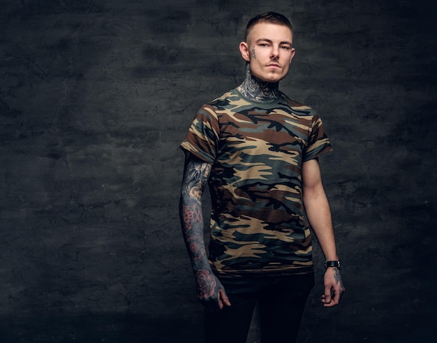 Free Photo a man with tattoos on his neck, face and arms, dressed in a camouflage t shirt.