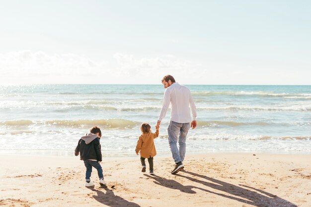 Man with toddlers walking towards sea