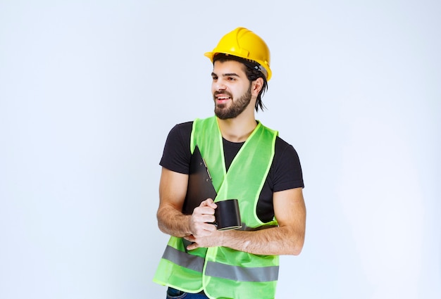 Man with yellow helmet holding project folder and a cup of coffee.