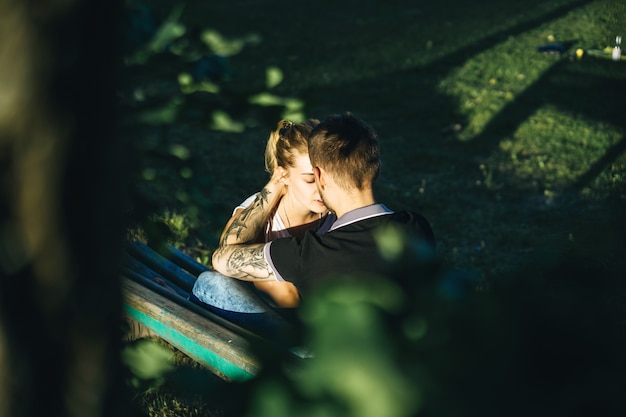 Free photo a man and a woman are sitting on a bench and kissing