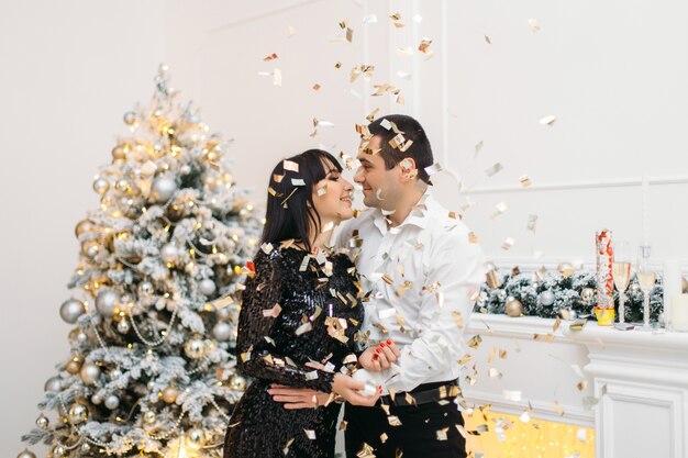 Man and woman dressed for a festive dinner stand before a shiny Christmas tree