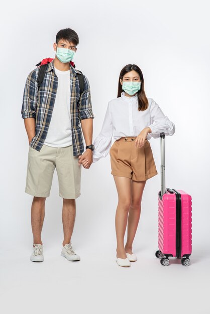 Man and woman dressed to travel, wearing masks along with luggage