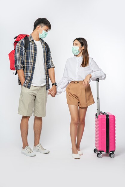 Man and woman dressed to travel, wearing masks along with luggage