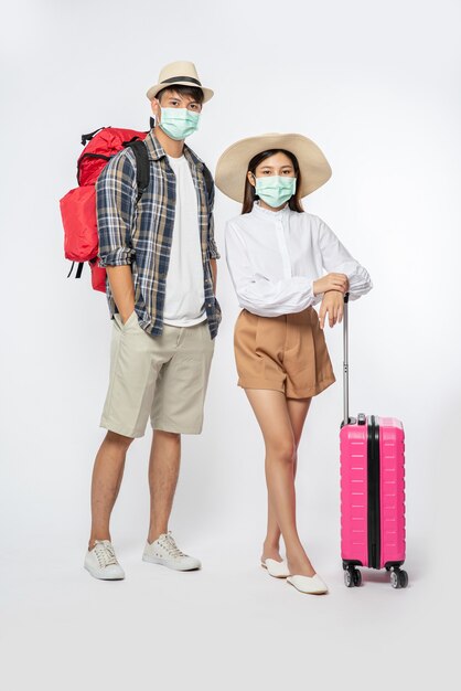 Man and woman dressed to travel, wearing masks along with luggage