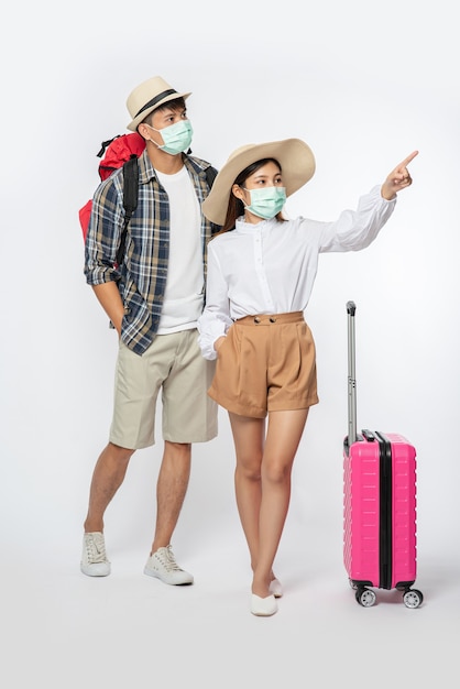 Man and woman dressed to travel, wearing masks along with luggage