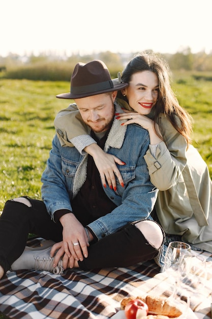 Man and woman in fashion clothes sitting on a nature on a picnic rug. Man wearing jacket and a black hat and woman coat