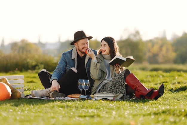 Man and woman in fashion clothes sitting on a nature on a picnic rug. Man wearing jacket and a black hat and woman skirt and red boots