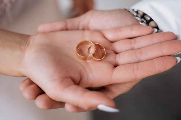 Man and woman hold two golden wedding rings on their arms