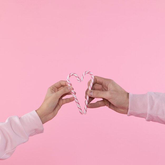 Man and woman holding candy canes in form of heart 