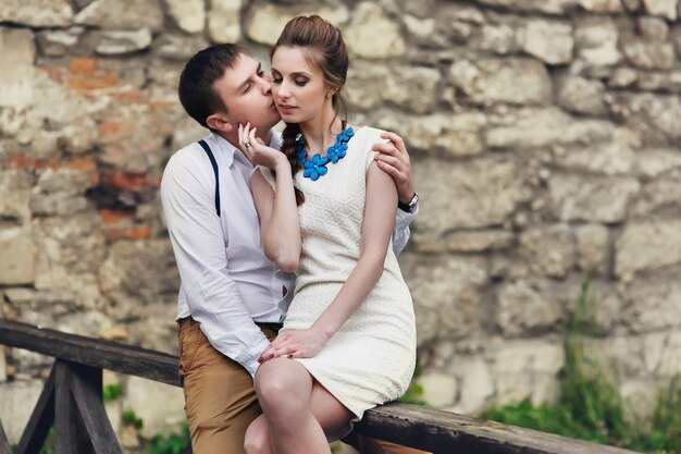 Man and woman kiss each other tender sitting on wooden handrails