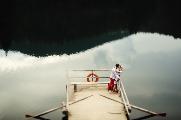 Free Photo man and woman kiss standing on wooden porch over mountain lake