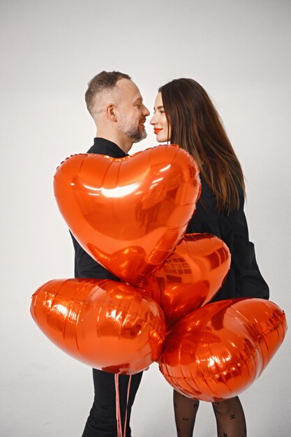 Free photo man and woman kissing covering with bunch of heartshaped red ballons