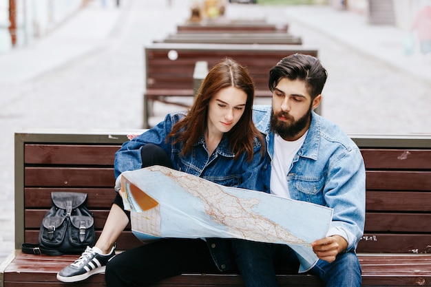 Man and woman look at the map sitting on the bench somewhere in an old city