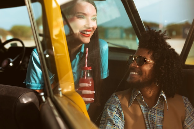 Man and woman posing in retro style with car and beverage