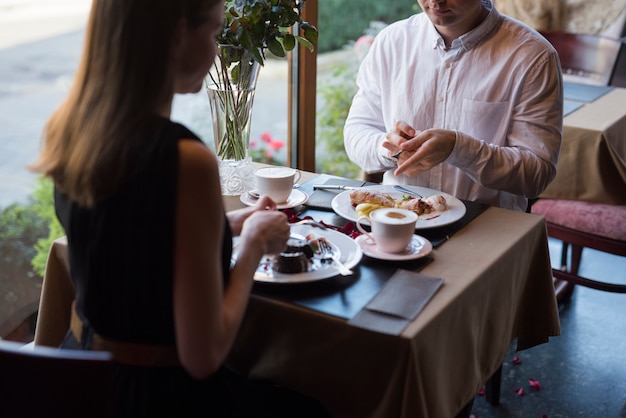 Free Photo man and woman sitting at table with desserts and drinks in cafe