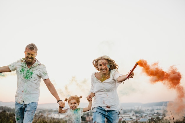 Man, woman and their little daughter have fun running with colorful smoke in their arms