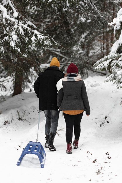 Man and woman walking into forest with sleigh from behind shot