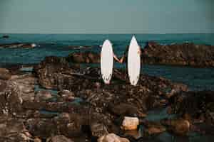 Free photo man and woman with surf boards holding hands on stone coast