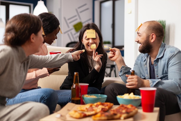 Free Photo man and women enjoying guessing game with sticky notes, playing charades together at drinks celebration after work hours. office workmates having fun with patnomime activity at party.