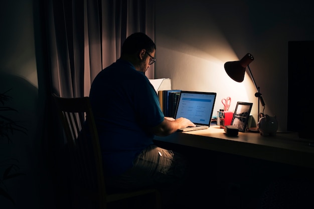 Free photo man working in a dark home office with a laptop