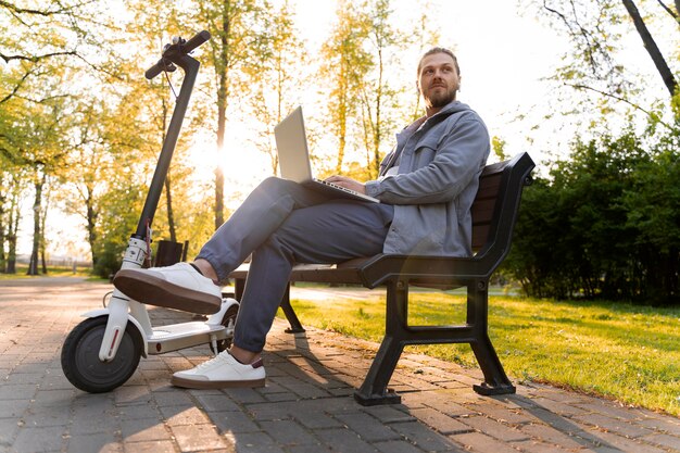 Man working on his laptop next to his scooter