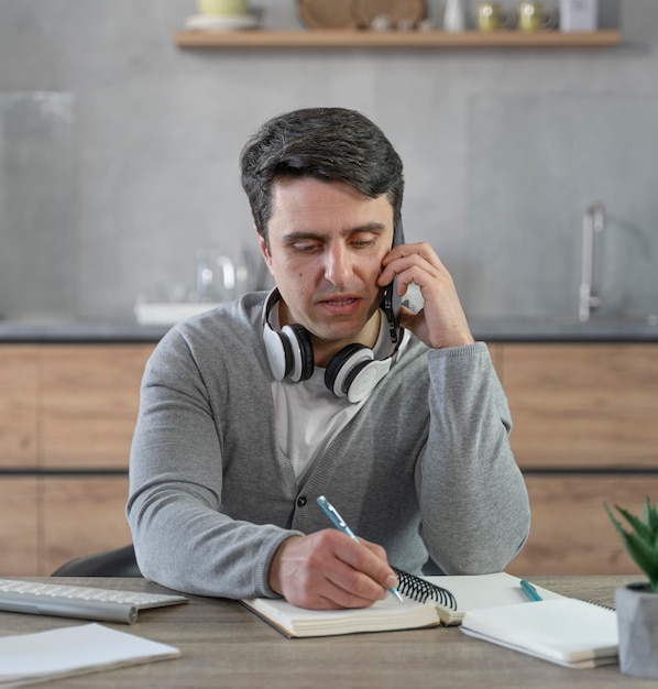 Man working in the media field having a phone call and writing stuff down on notebook