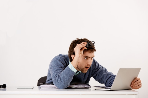 Free Photo man working in office, take-off glasses and staring confused with disbelief laptop screen, reading shocking news, receive curious report