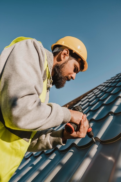 Free photo man working on roof with a drill low view